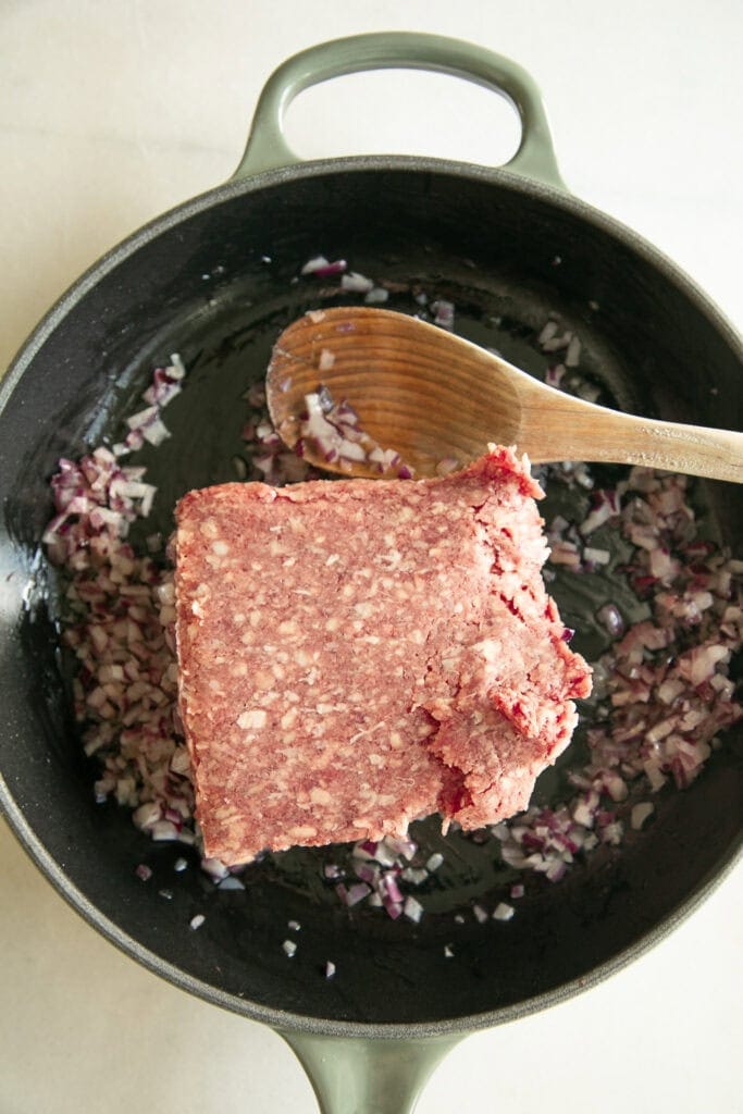 raw ground beef in a skillet with sautéed onions