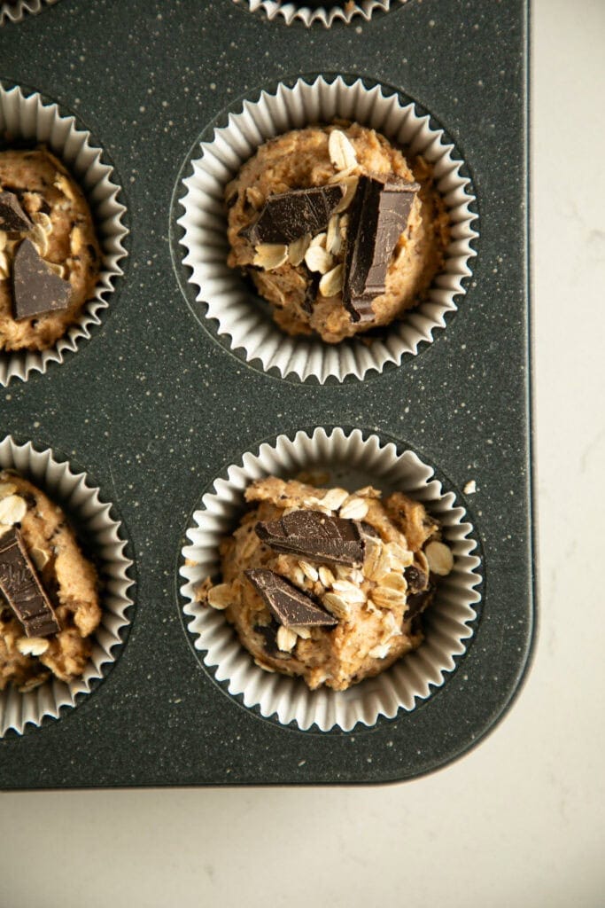 muffin batter scooped into a muffin tin topped with extra chocolate