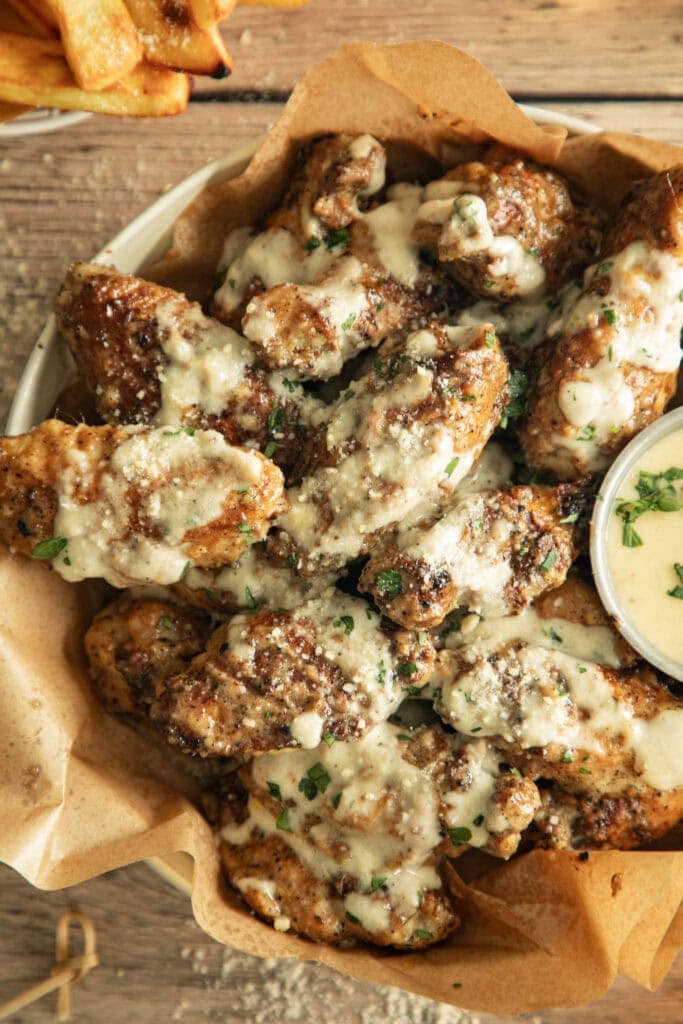 bowl full of pan fried chicken wings with a side of sauce