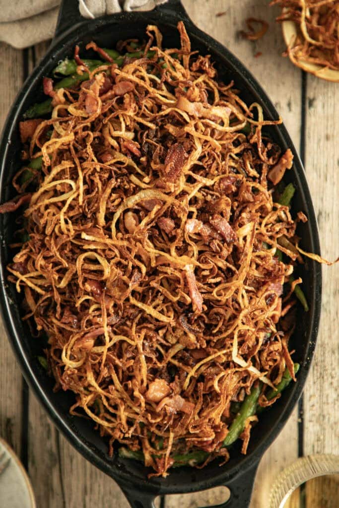 Oval casserole dish loaded with green bean casserole and topped with crispy onion straws. 
