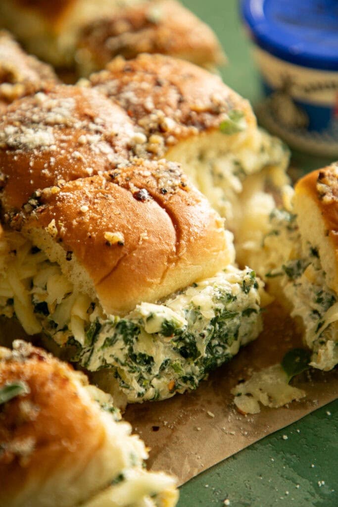 Side shot of loaded spinach artichoke dip sliders topped with garlic butter