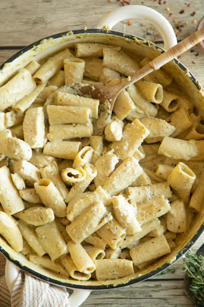 Sauces rigatoni noodles in a pan tossed with chicken and basil cream sauce.
