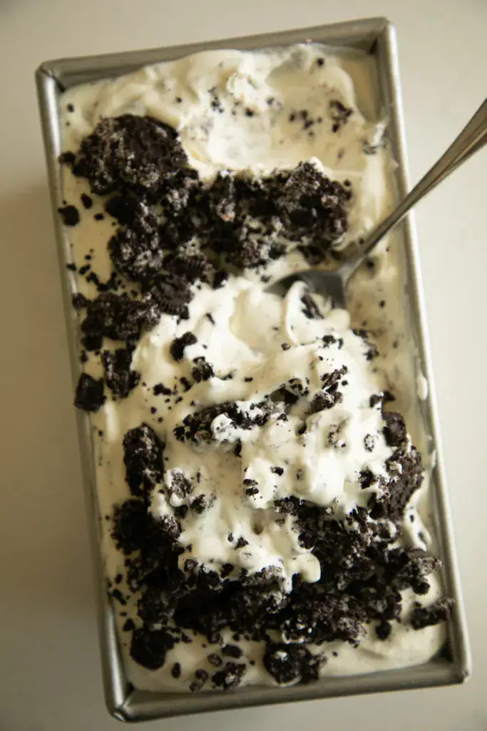 Metal loaf pan full of Oreo ice cream with a spoon and crumbled Oreo cookies