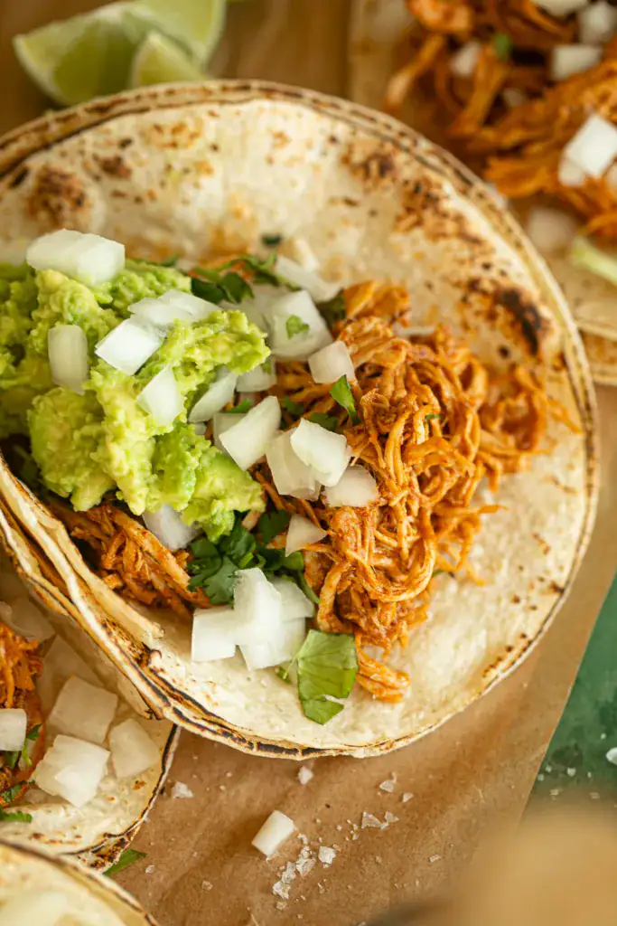 charred corn tortilla topped with shredded taco chicken, diced onions, cilantro, and guacamole 