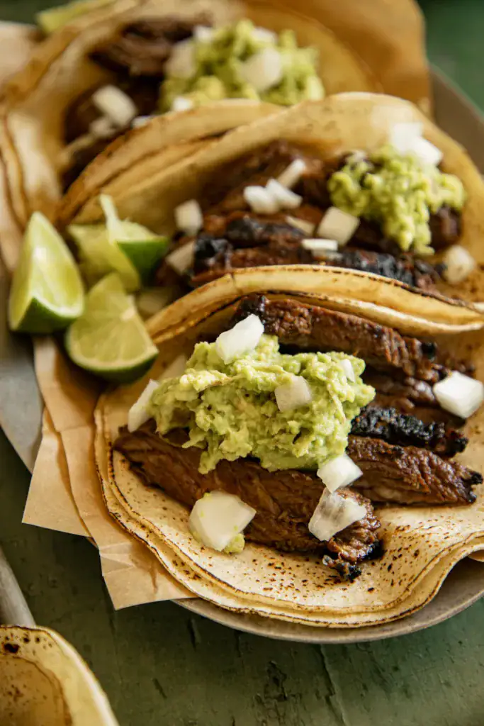 charred corn tortillas on a platter loaded with skirt steak, guacamole and onions.