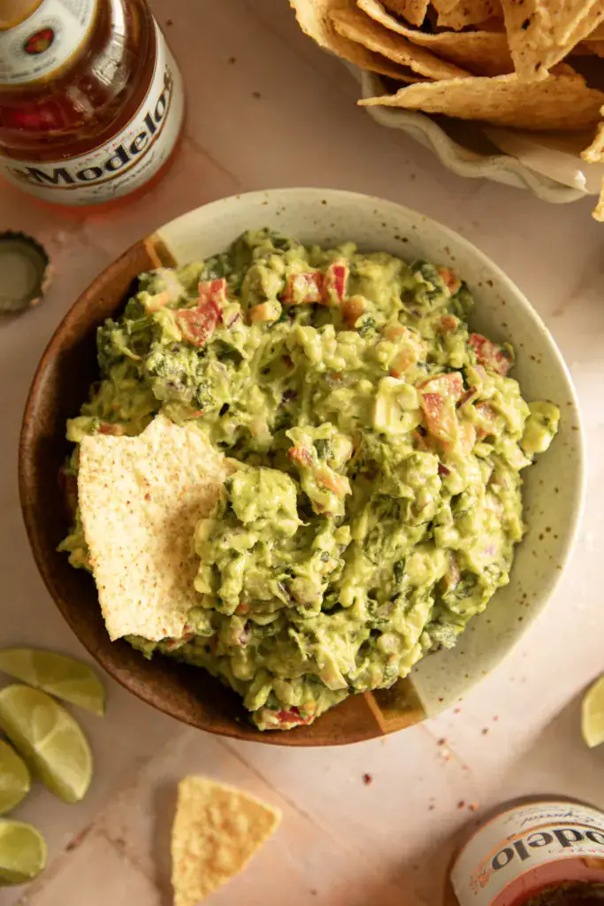 Round speckled bowl full of fresh guacamole on a pink background
