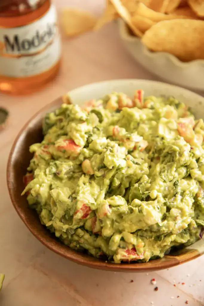 ceramic bowl full of guacamole with a modelo in the back ground
