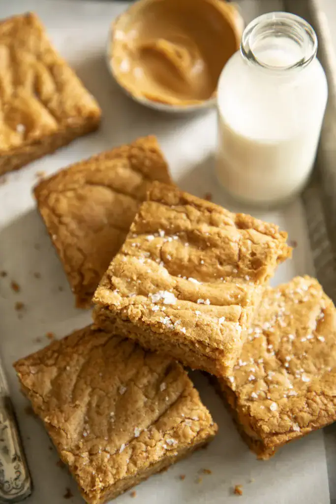 Peanut butter cookie bars sprinkled with sea salt, styled with a vintage knife and glass of milk