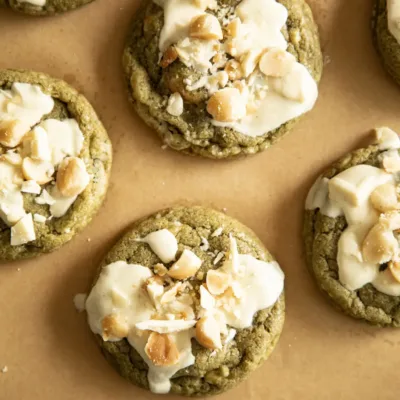 Close-up of freshly baked matcha cookies with melted white chocolate and chopped macadamia nuts on parchment paper