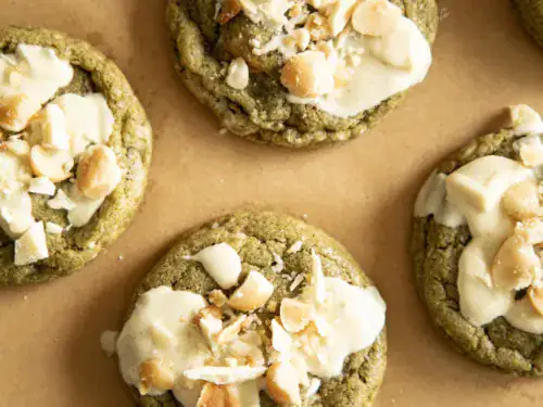 Close-up of freshly baked matcha cookies with melted white chocolate and chopped macadamia nuts on parchment paper