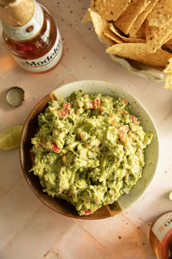 Fresh guacamole in a bowl next to a bowl of corn tortilla chips