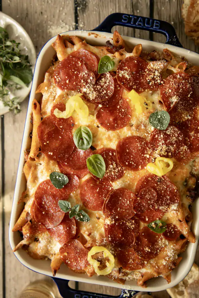 Overhead shot of loaded pepperoni pasta casserole in a Staub baking dish, sprinkled with parmesan and basil