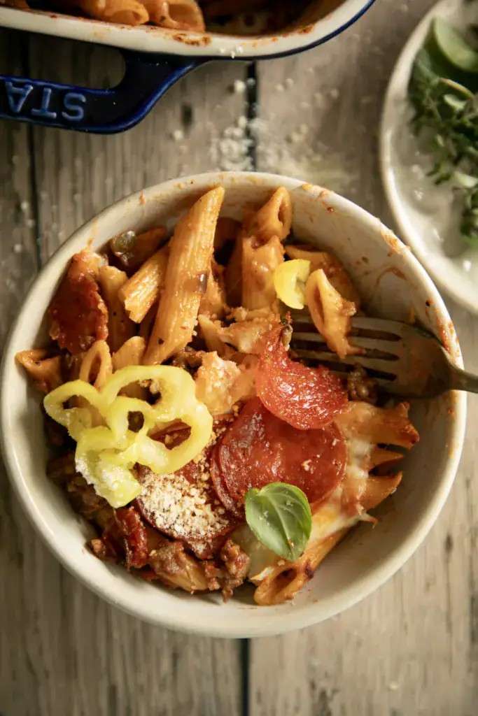 Bowl of pepperoni pizza pasta bake topped with banana peppers and fresh basil