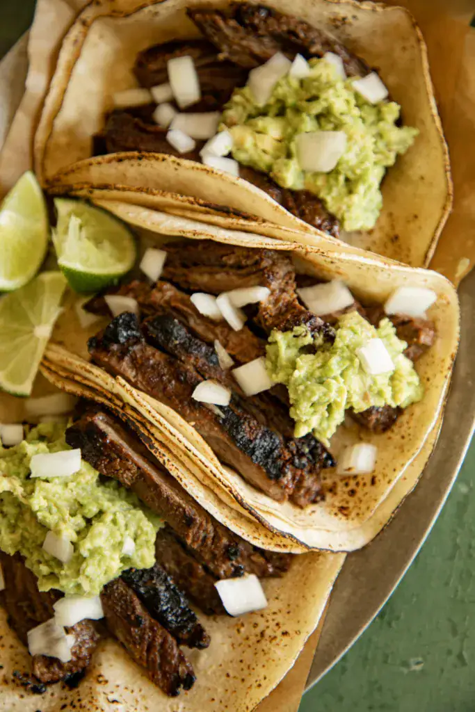 charred corn tortillas filled with sliced steak and topped with guacamole and onion
