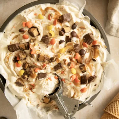 Pan of no-churn peanut butter cup ice cream with candy pieces and ice cream scoop