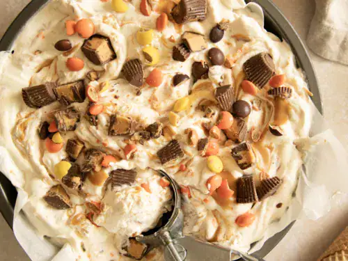 Pan of no-churn peanut butter cup ice cream with candy pieces and ice cream scoop