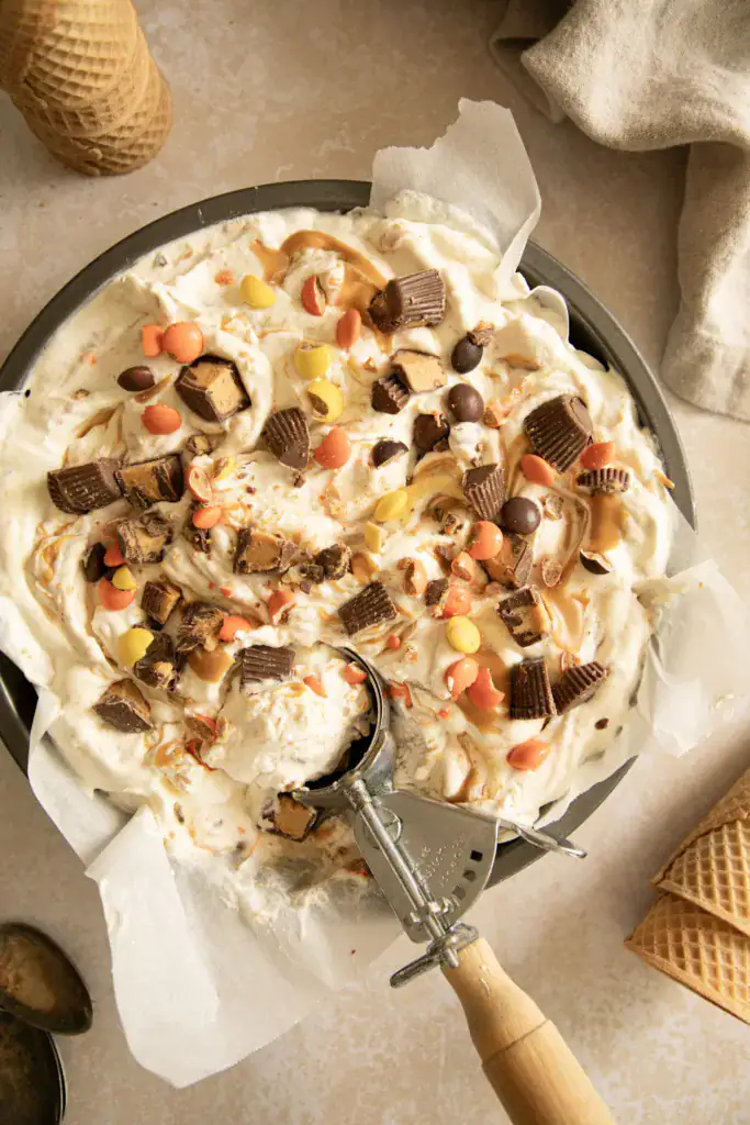 Pan of no-churn peanut butter cup ice cream with candy pieces and ice cream scoop