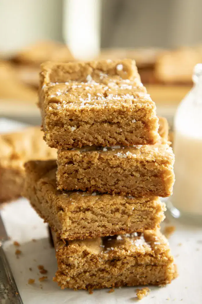 Stack of fudgy peanut butter cookie bars sprinkled with flaky sea salt on parchment paper