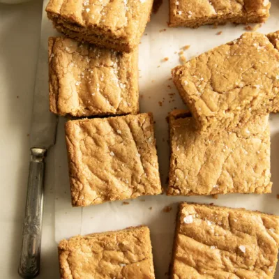 Peanut butter cookie bars sprinkled with sea salt, styled with a vintage knife and glass of milk