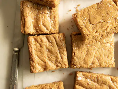 Peanut butter cookie bars sprinkled with sea salt, styled with a vintage knife and glass of milk