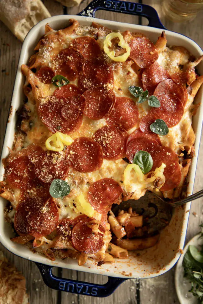 Serving spoon inside baked pepperoni pasta casserole, showing cheesy pasta layers