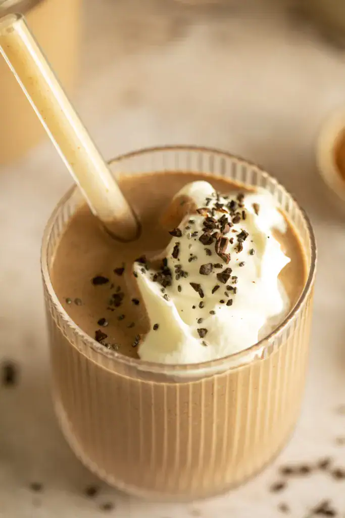 Close-up of a chocolate banana smoothie topped with whipped cream, chia seeds, and chocolate shavings.