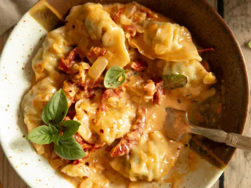 Bowl of baked dumplings with a fork resting inside, coated in a creamy tomato-basil sauce.