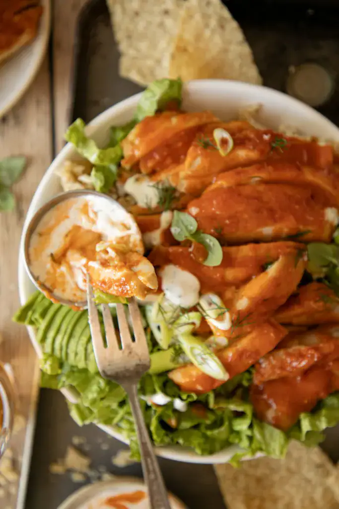 Forkful of buffalo chicken dipped in ranch over salad bowl