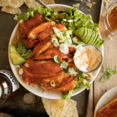Close up of sliced buffalo chicken thighs on lettuce and rice