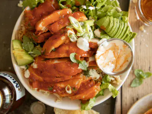 Close up of sliced buffalo chicken thighs on lettuce and rice