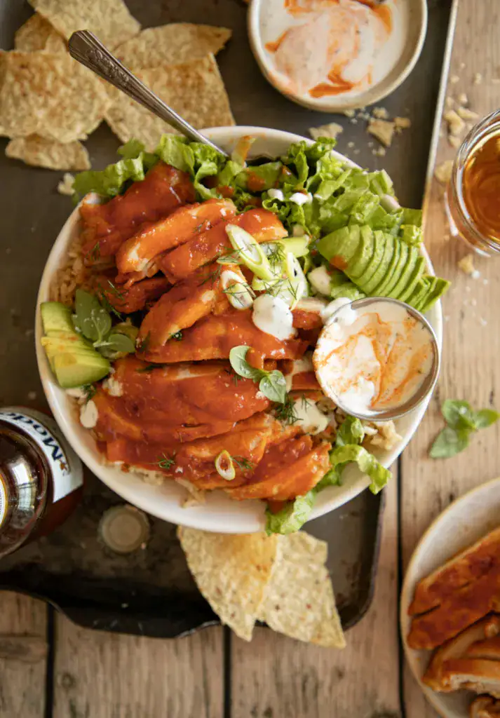 Close up of sliced buffalo chicken thighs on lettuce and rice