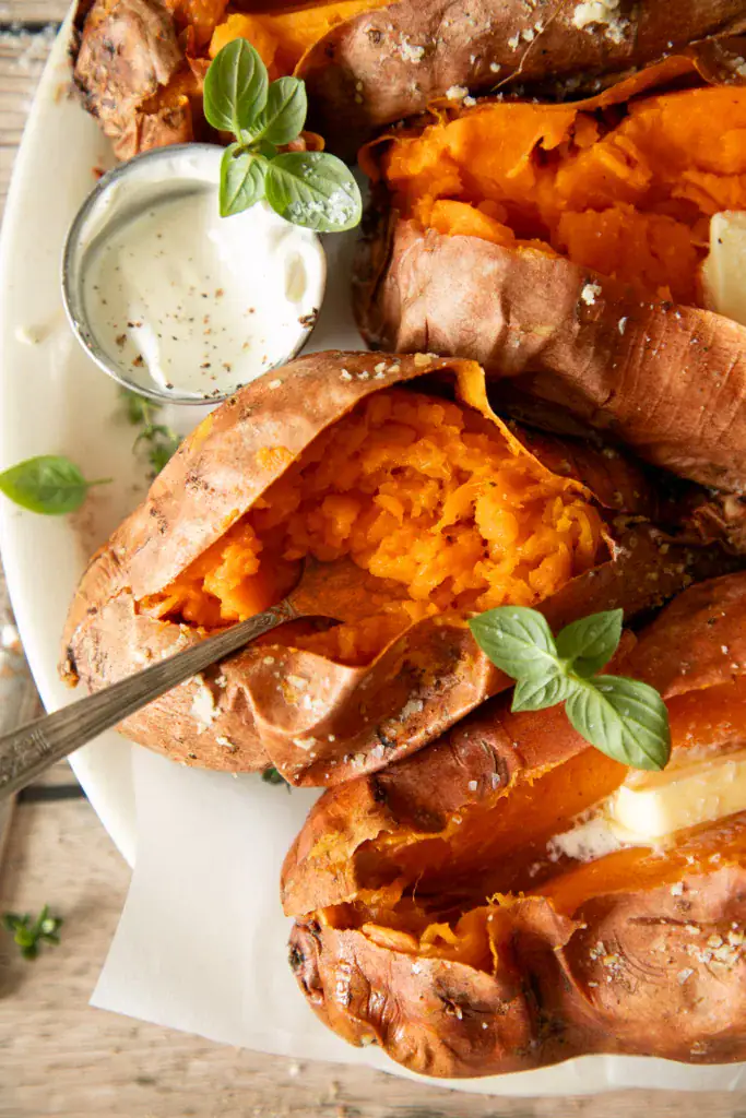 Spoon breaking into a soft, grilled sweet potato on a serving platter.