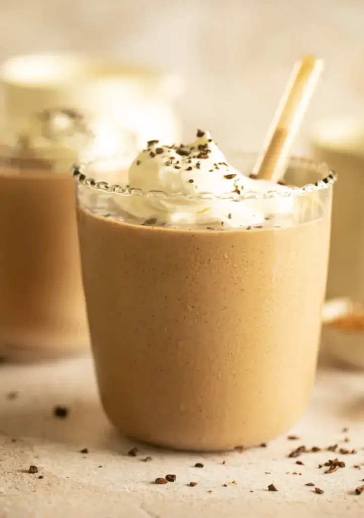 Thick chocolate smoothie in a clear glass with scalloped edge, topped with whipped cream.