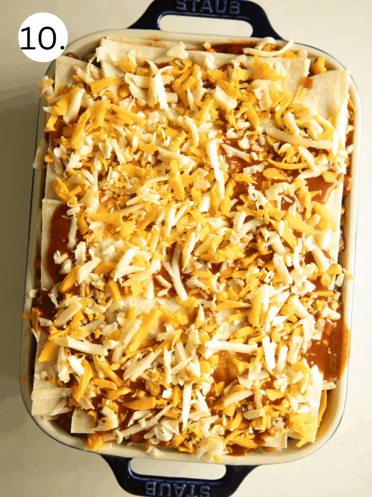 Assembled baking dish of Mexican lasagna topped with shredded cheese and enchilada sauce before going into the oven.