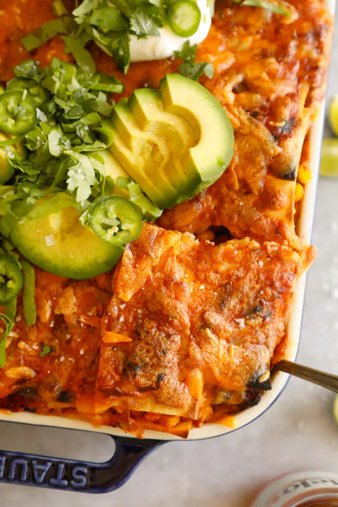 Spatula scooping a portion of Mexican lasagna from the baking dish, showing the cheesy filling and toppings.
