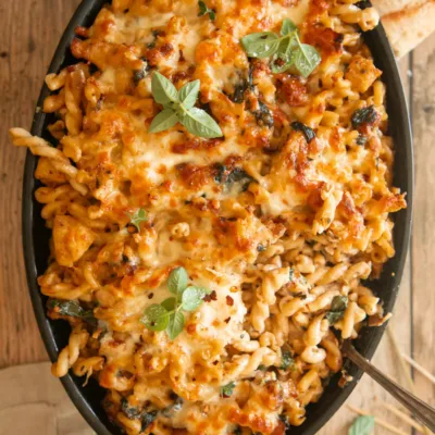 Spoonful of baked pasta being served from the dish, showing cheesy spirals and chunks of chicken.