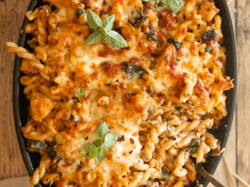 Spoonful of baked pasta being served from the dish, showing cheesy spirals and chunks of chicken.