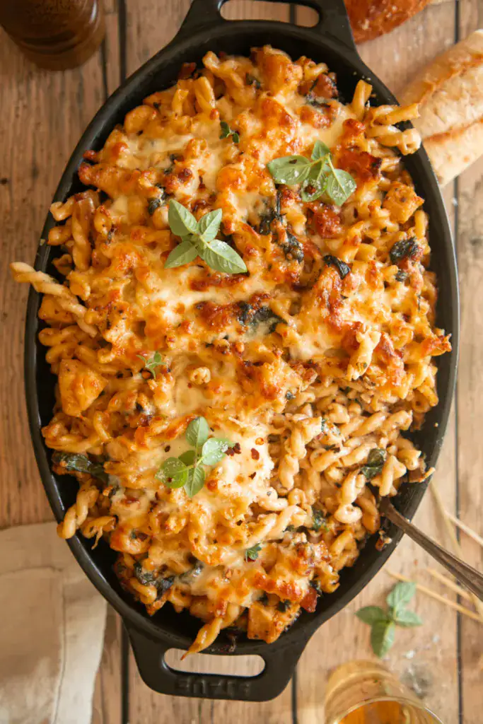 Spoonful of baked pasta being served from the dish, showing cheesy spirals and chunks of chicken.