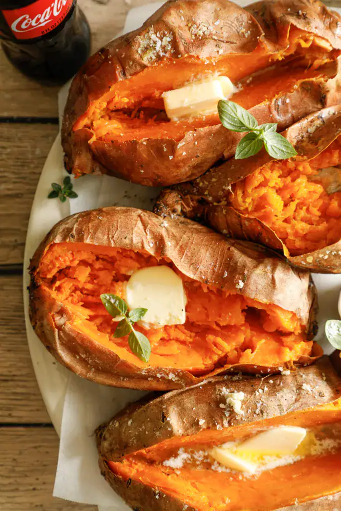 Split sweet potatoes with melted butter and salt, served on a white platter with herbs.