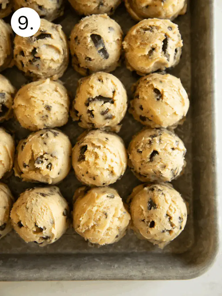 Scoops of chocolate chip cookie dough arranged on a baking sheet.