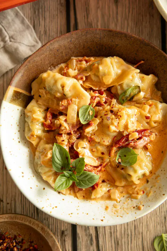 A bowl of creamy baked dumplings garnished with basil, showing the saucy texture and hearty ingredients.