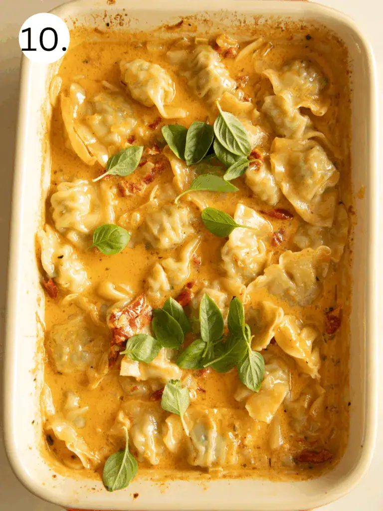 Baked dumplings in creamy sauce topped with fresh basil leaves in a casserole dish.