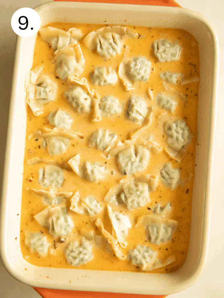 Baking dish filled with dumplings arranged in a creamy tomato sauce before baking.