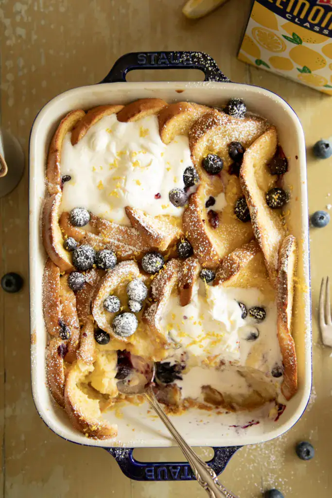 blue casserole dish with baked lemon French toast and a scoop taken out 