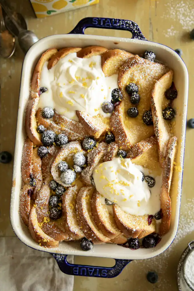 blue casserole dish full of baked French toast topped with blueberries and whipped cream