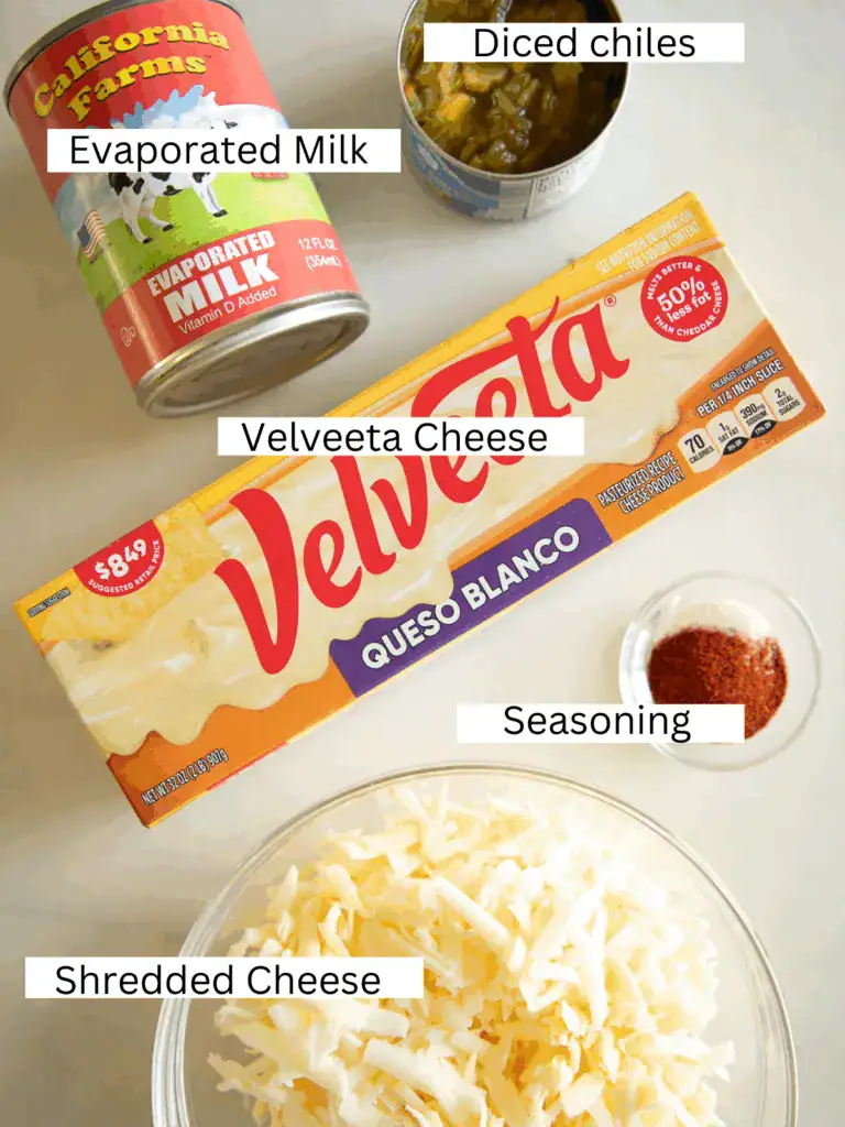 Shredded cheese, Velveeta, green chiles, spices, and milk in a slow cooker before cooking.
