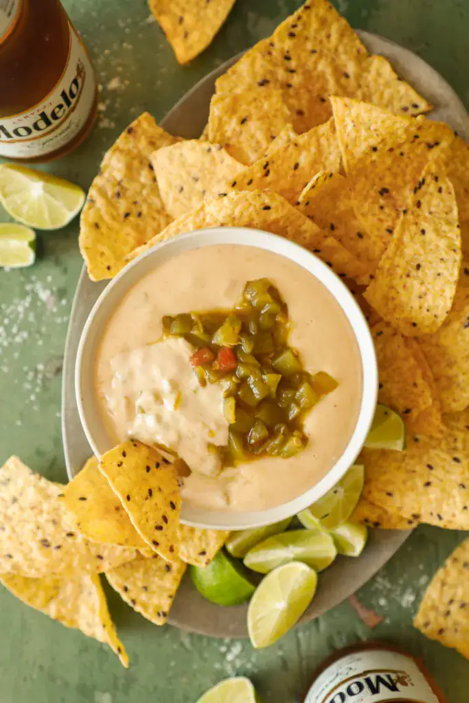 Queso dip scooped with a tortilla chip, showing creamy texture and green chile topping.