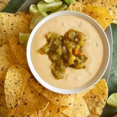 Overhead shot of queso dip surrounded by chips, lime wedges, and bottles of Modelo beer.