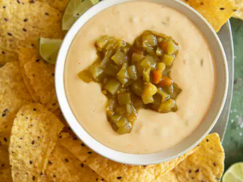 Overhead shot of queso dip surrounded by chips, lime wedges, and bottles of Modelo beer.