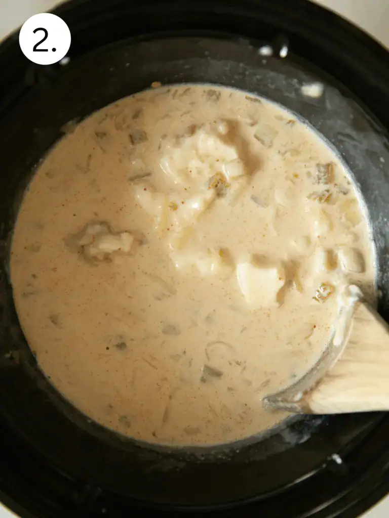Cheese mixture partially melted in a slow cooker with visible green chiles and seasonings.